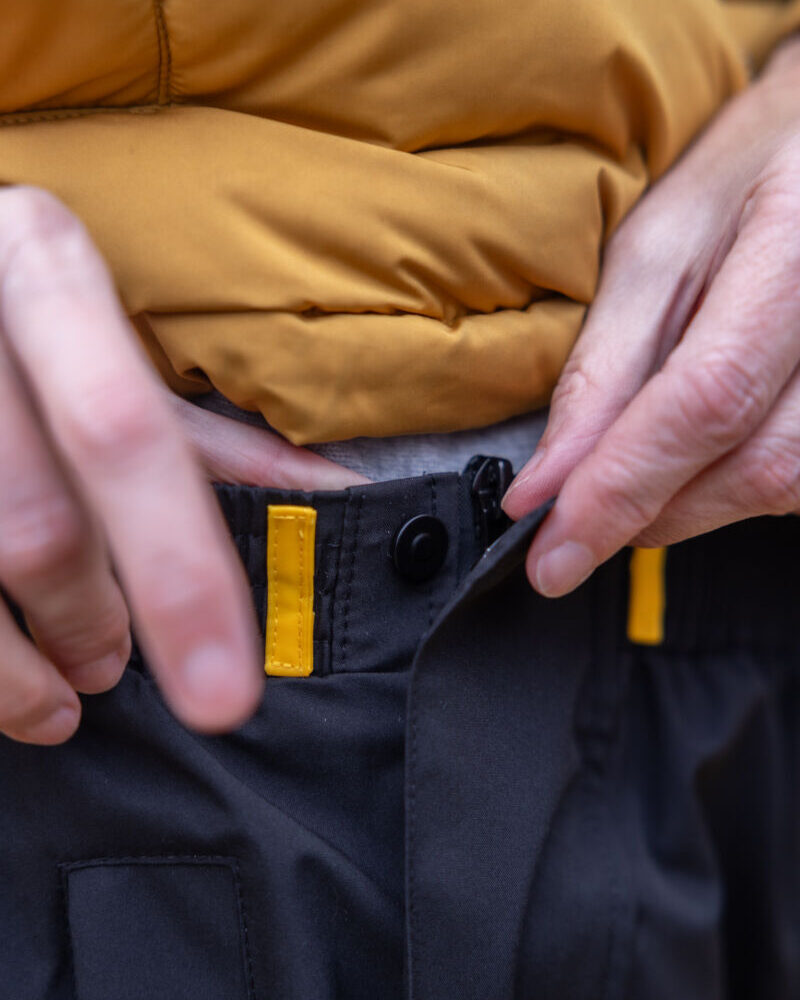 Close-up van vrouw die de regenbroek van Hello Rain sluit met de handige knopen.